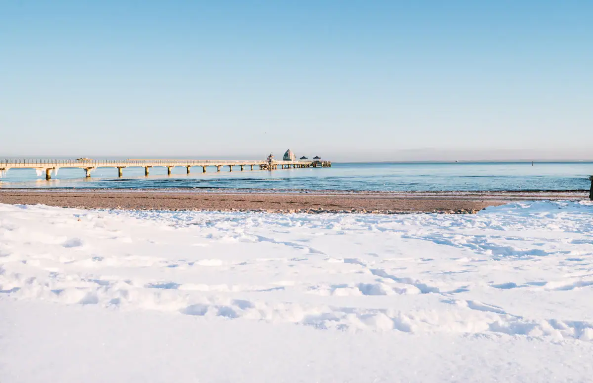 Strand Winter Schneebedeckter Strand mit Steg und Gewässer im Winter.