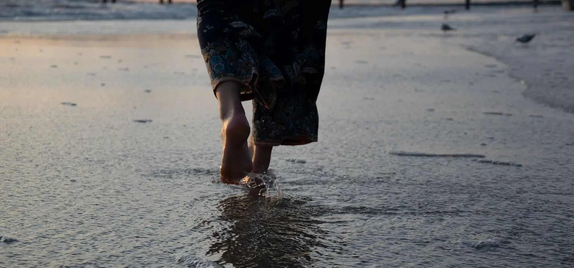 Person läuft barfuß am Strand entlang.