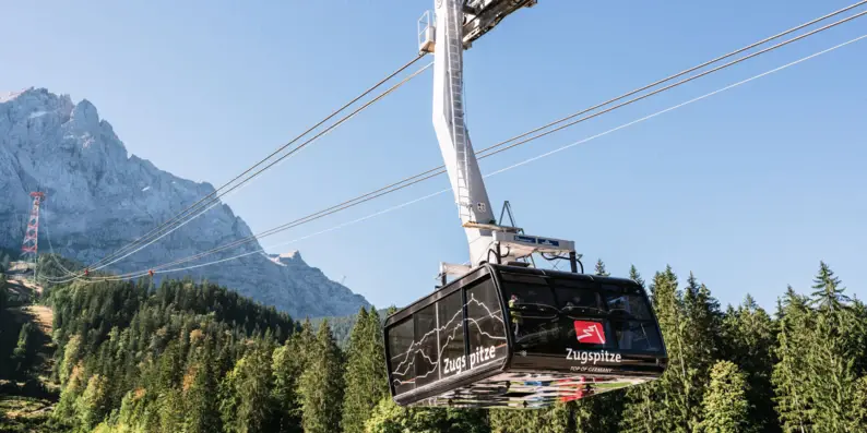 Die Zugspitz Seilbahn mit Bäumen und Bergen im Hintergrund.