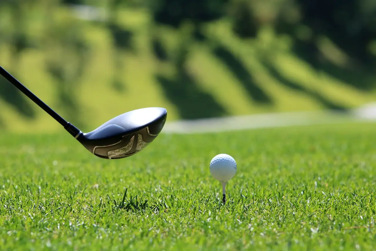 Golfschläger und Ball auf einem Abschlag im Gras.