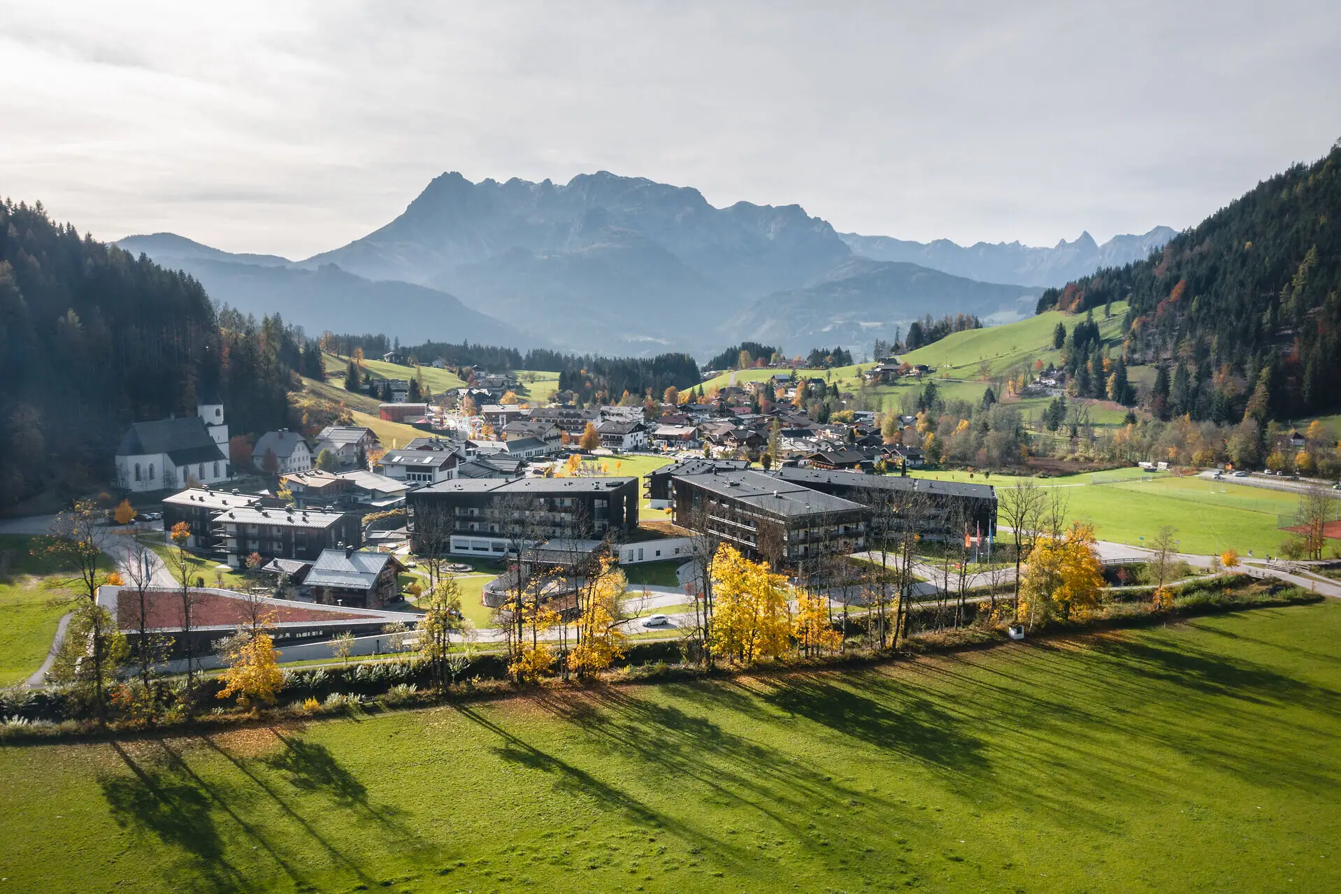 Stadt im Tal mit Bergen im Hintergrund, umgeben von Graslandschaft und Bäumen.