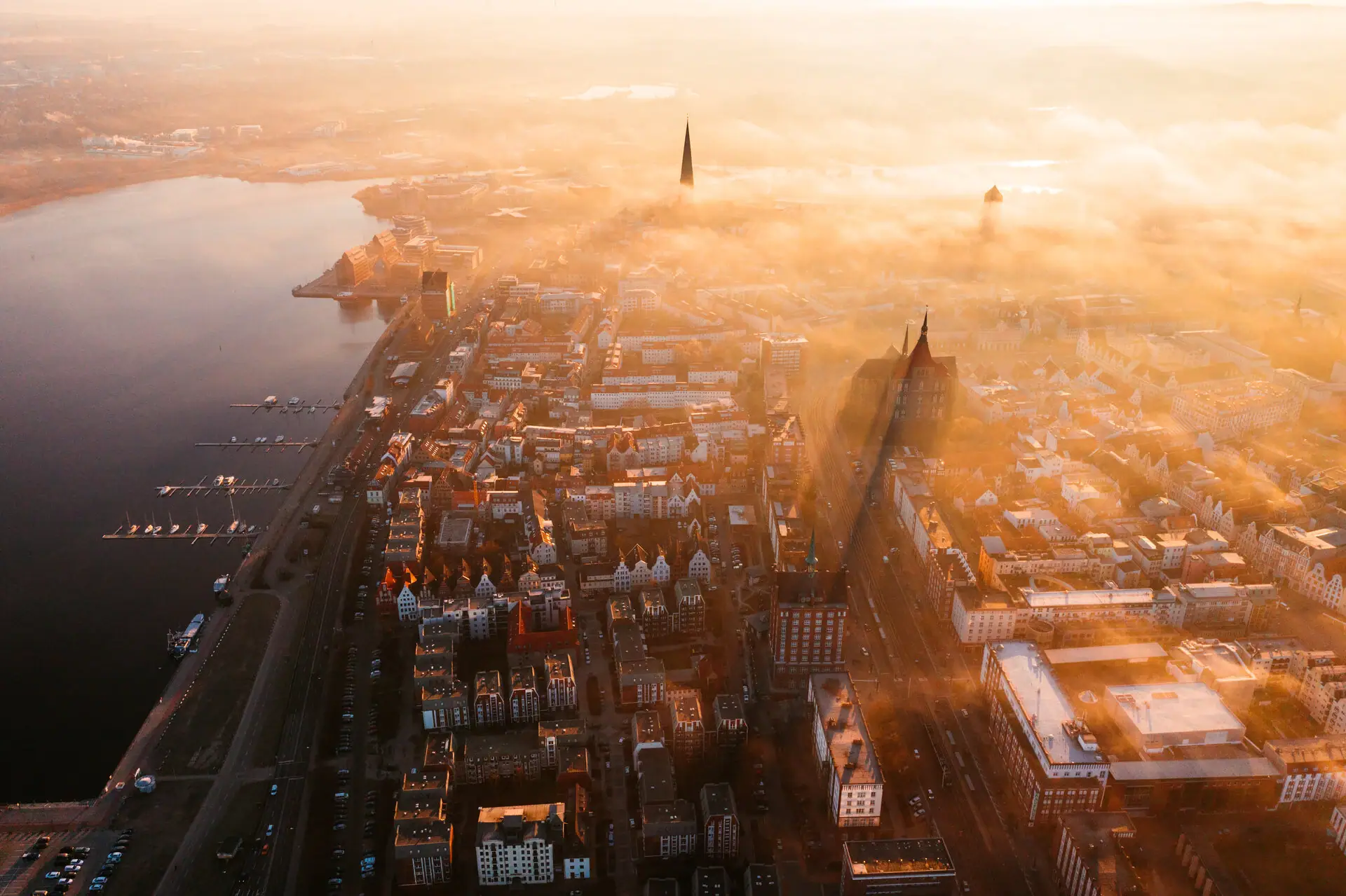 Vogelperspektive auf eine neblige Stadt mit Gewässer im Vordergrund.