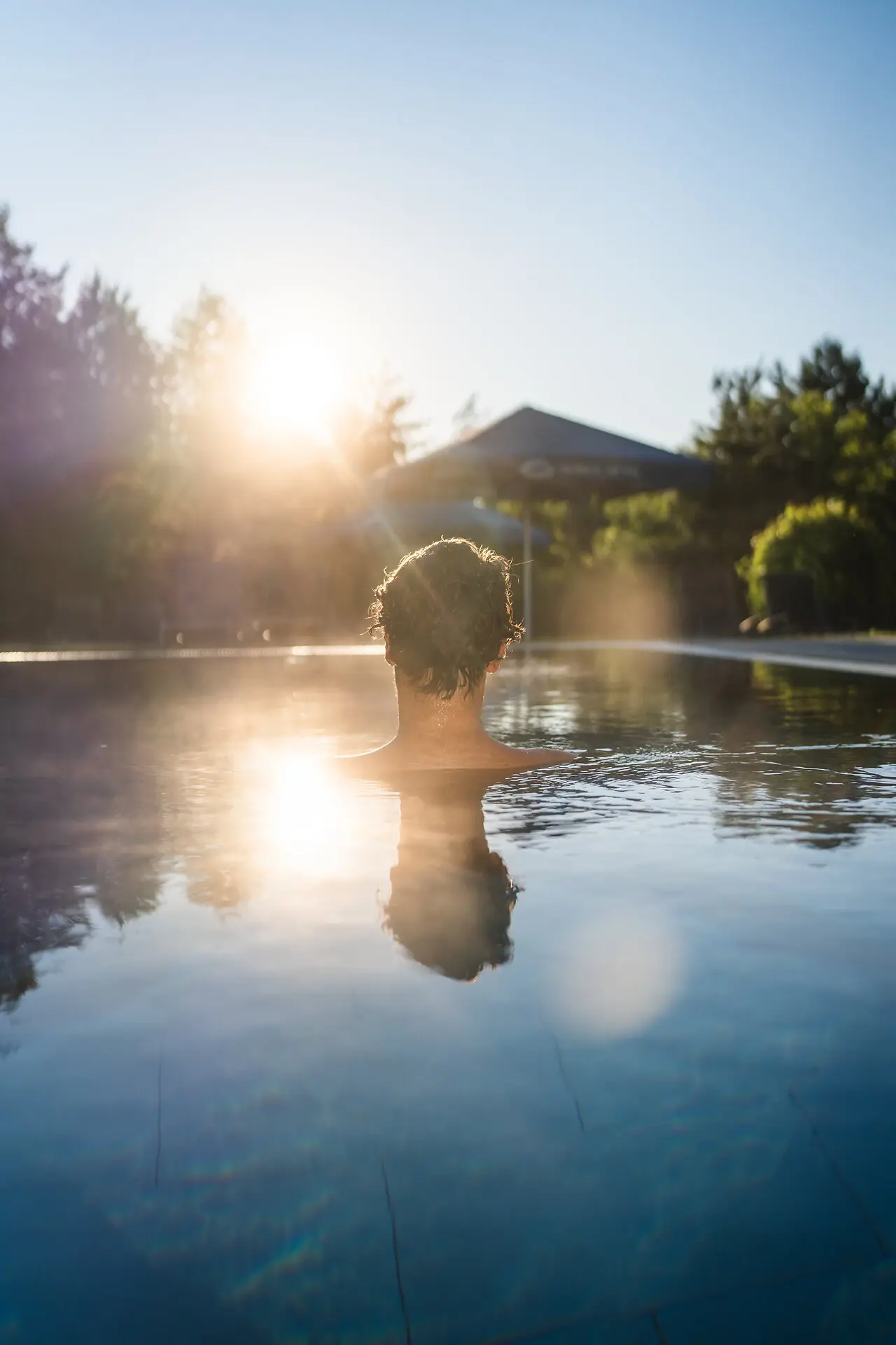 Person swimming in a pool under the sunlight with trees in the background