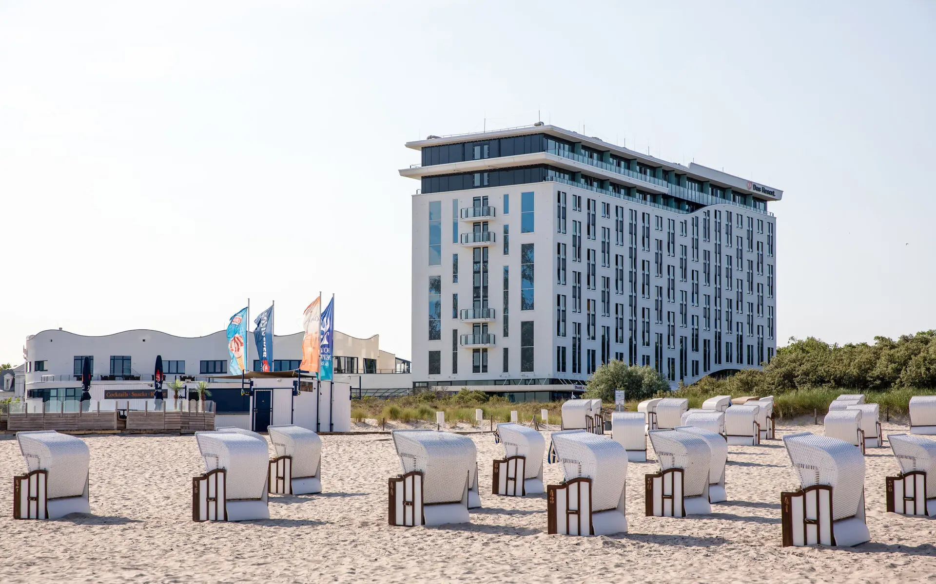 Hinter einem Strand mit vielen Strandkörben steht ein weißes Hotelgebäude. 