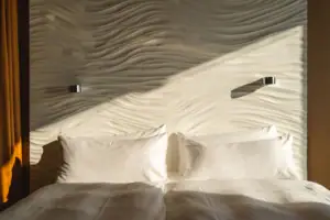 Zimmer im aja Warnemünde Ein Bett mit Kissen vor einer beleuchteten Wand.