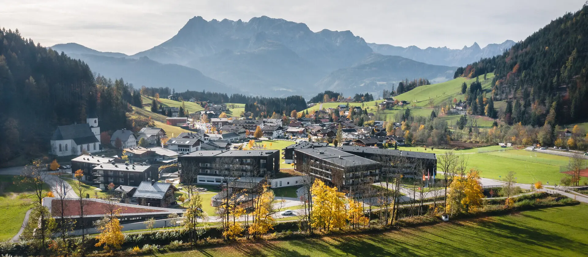Ein Dorf in einem Tal mit Bergen im Hintergrund und blauem Himmel.