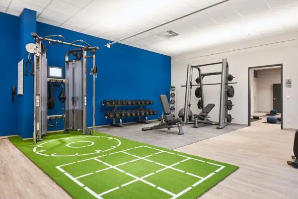 Fitnessstudio mit Trainingsgeräten und grünem Teppichboden