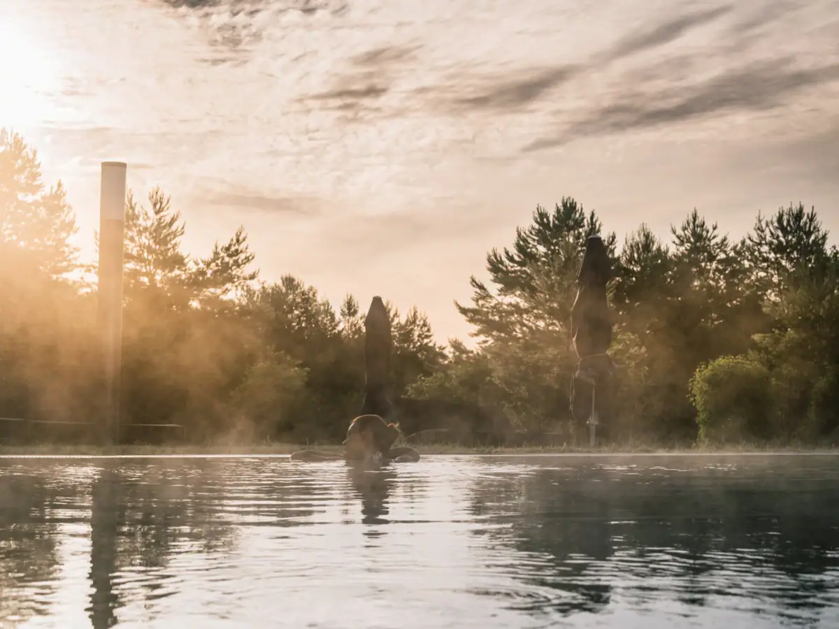 Eine Frau schwimmt in einem Außenpool mit Bäumen und bewölktem Himmel.