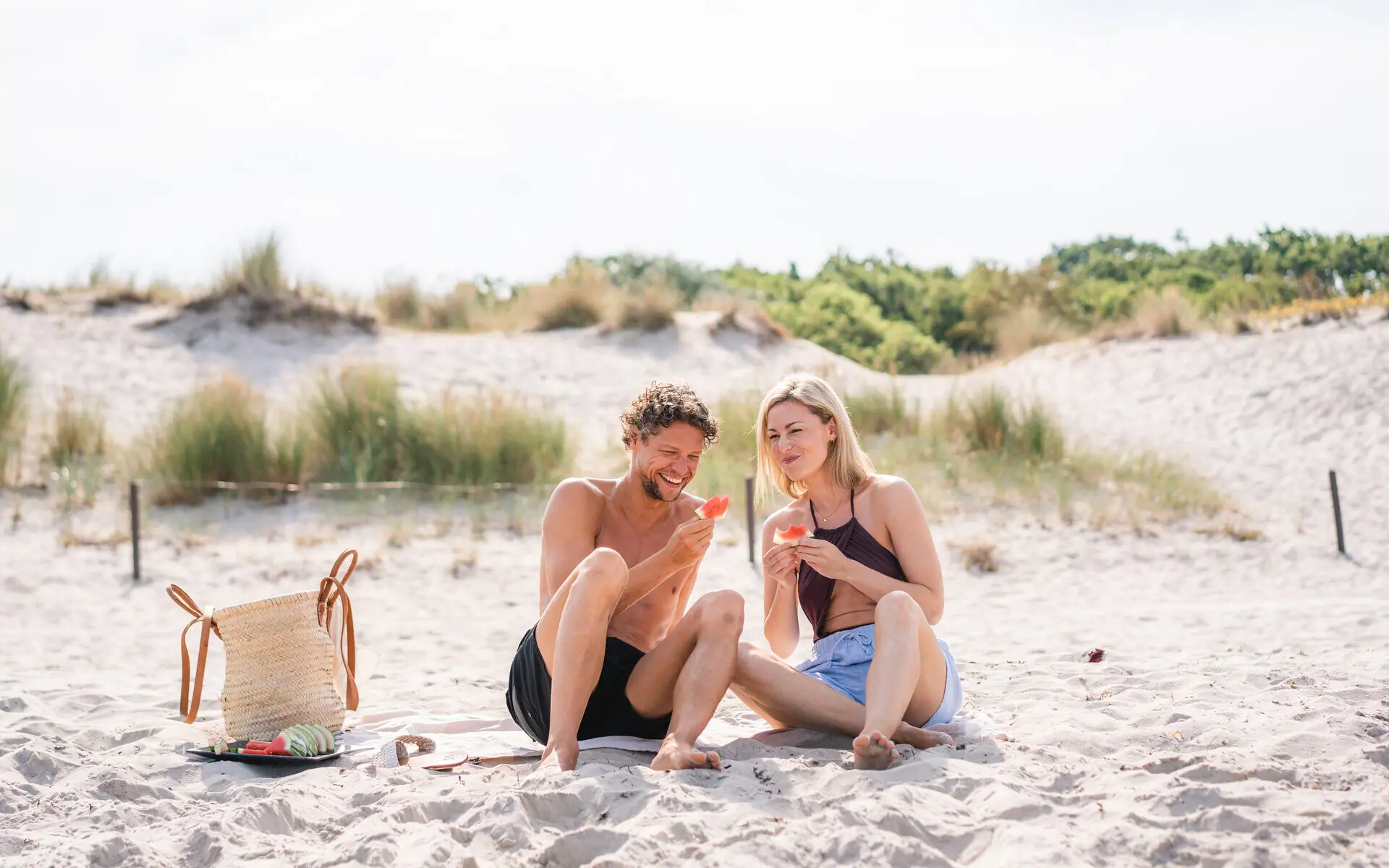 Ein Paar sitzt glücklich am sonnigen Ostseestrand und genießt Wassermelone. 