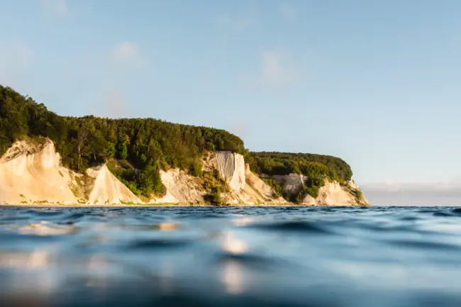 Kreidefelsen auf Rügen Körper aus Wasser mit Klippe und Bäumen im Hintergrund.