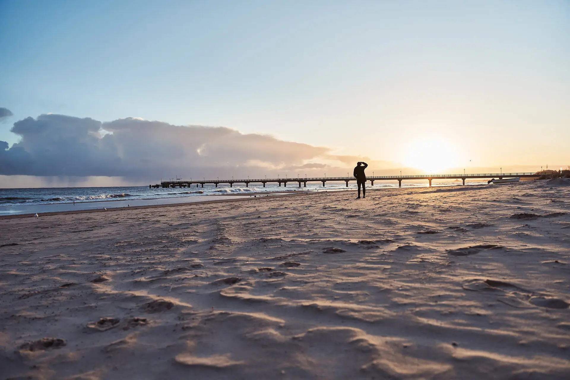 Eine Person geht am Strand entlang bei Sonnenuntergang.