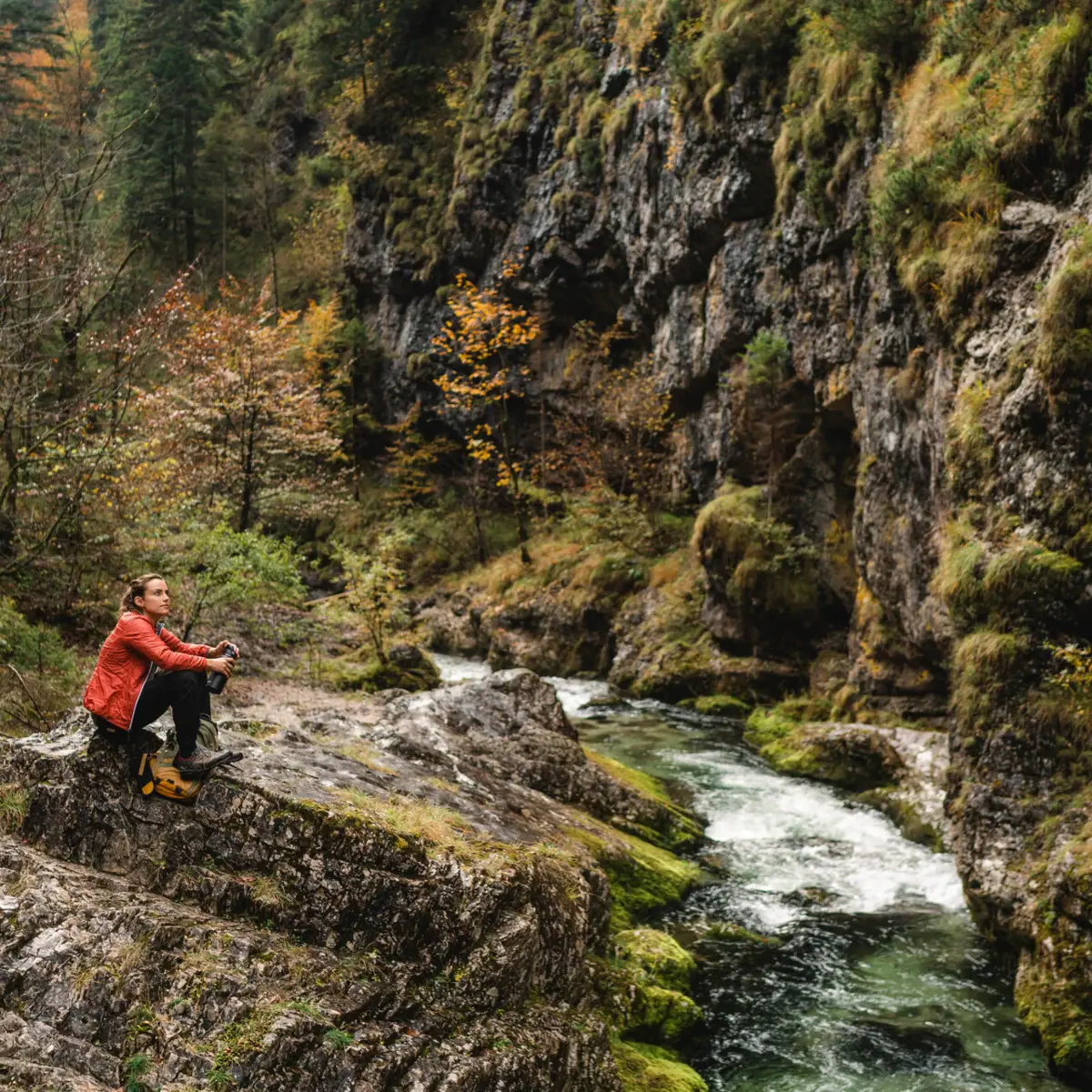 Eine Frau sitzt auf einem Felsen am Fluss in der Weißbachschlucht.