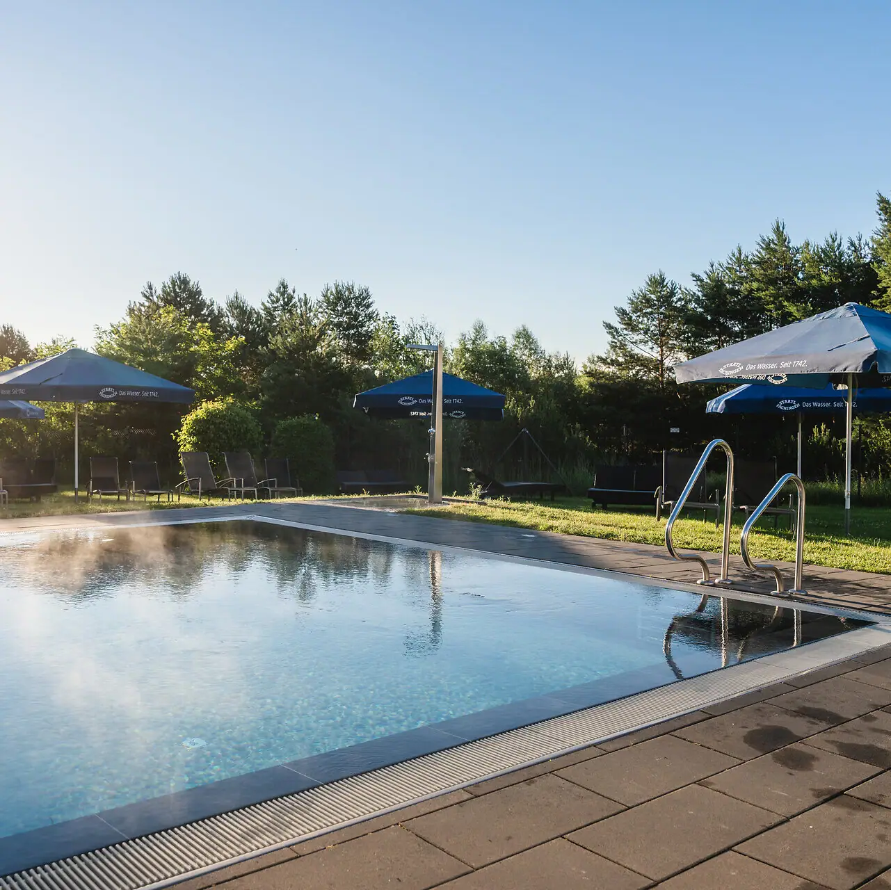 Ein Außenpool mit Sonnenschirmen und umgebendem Gras.