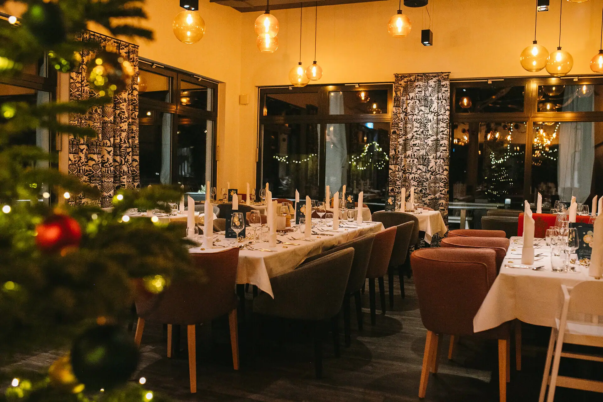 Ein Raum mit Tischen und Stühlen, festlich dekoriert und im Vordergrund in der Unschärfe steht ein Weihnachtsbaum.