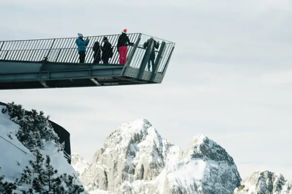 Menschen stehen auf einer Brücke über einem verschneiten Berg.