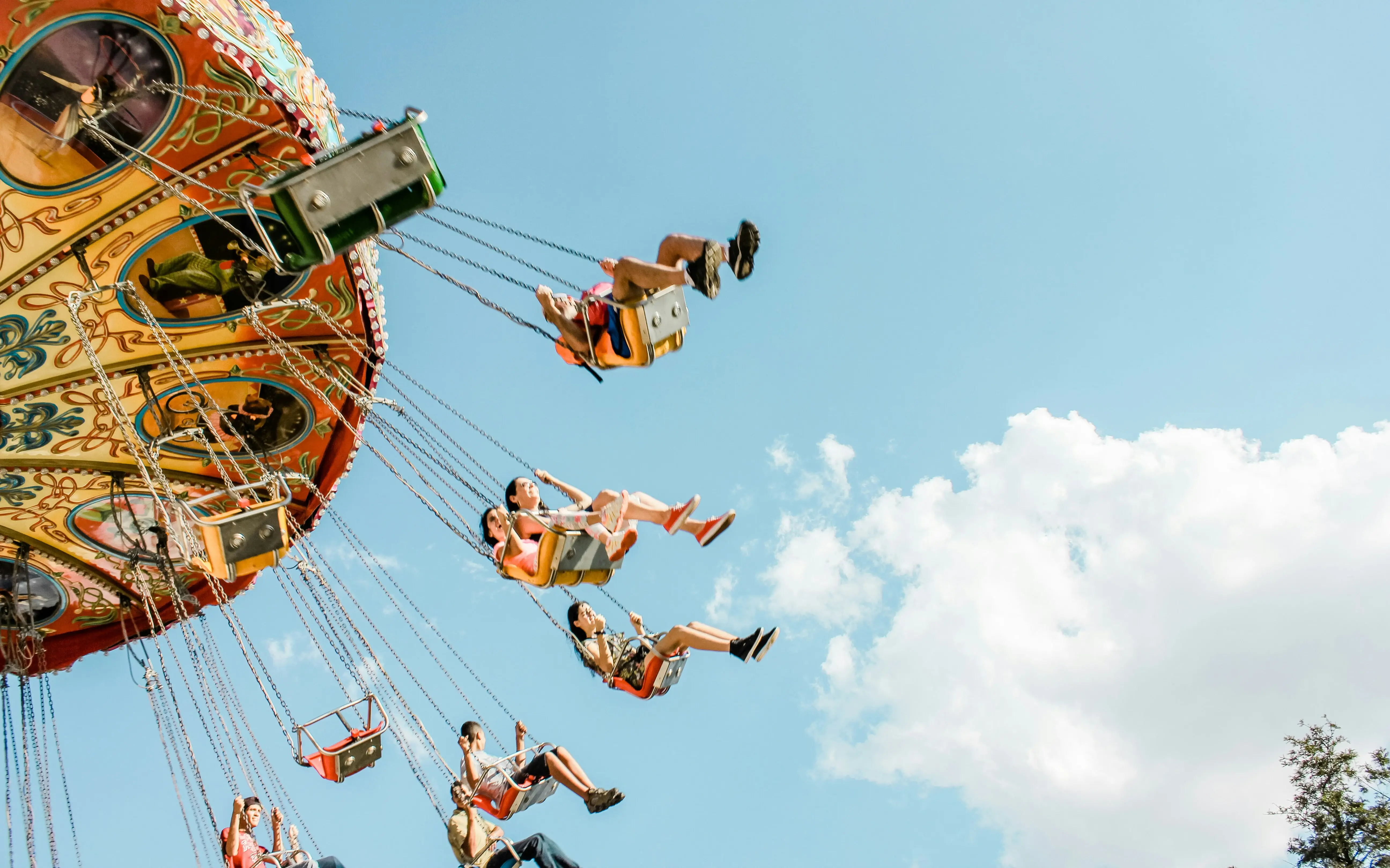 Fröhliche Kinder fliegen in den Sitzen eines Kettenkarussells durch die Luft. Das Karussell hat bunte Muster und de Himmel strahlt blau.  