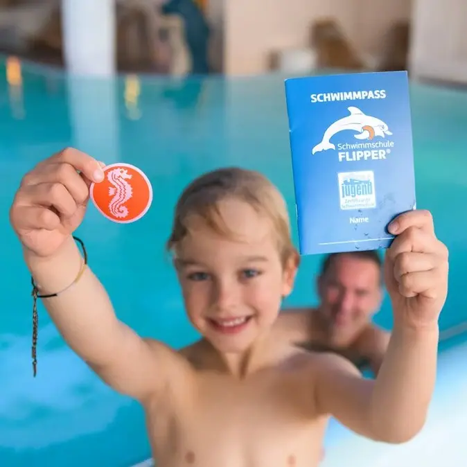 Ein Junge hält ein Buch und eine Münze im Pool.