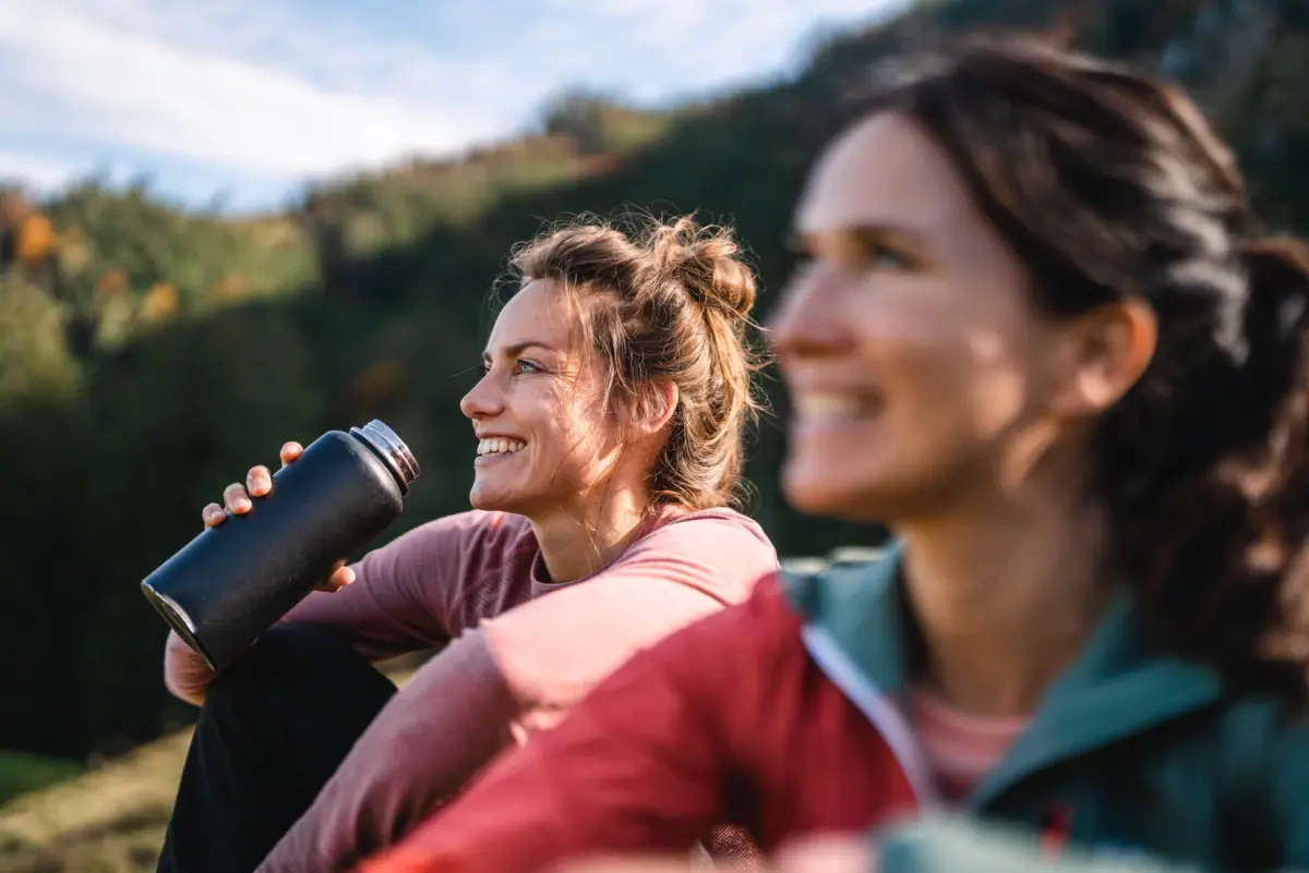 Zwei Frauen sitzen nebeneinander im Freien und lächeln.