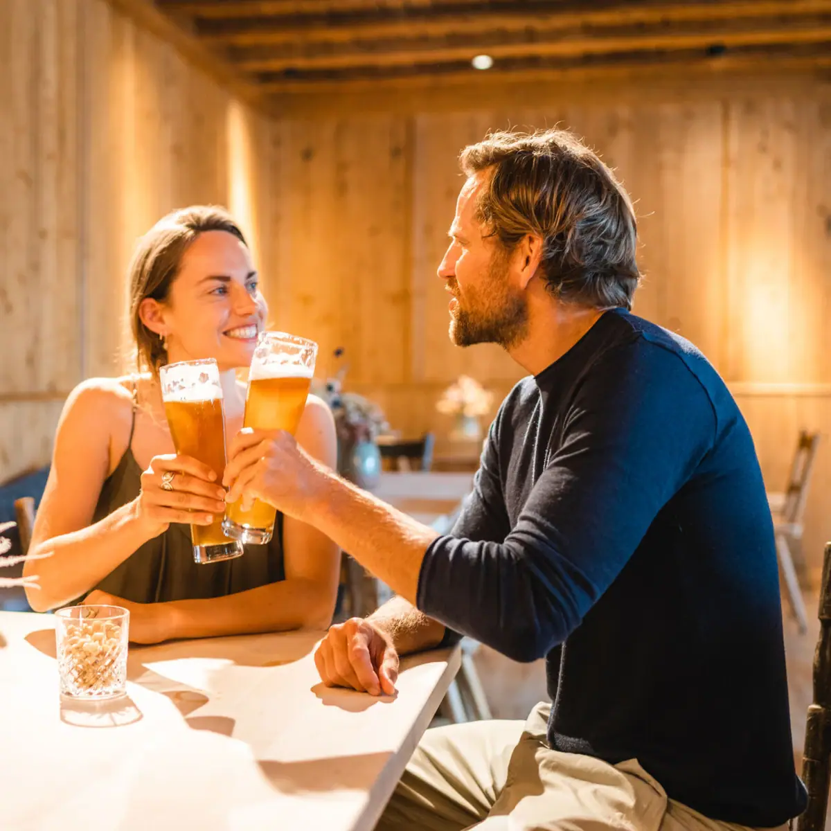 Anstoßen mit Bier Ein Mann und eine Frau sitzen an einem Tisch mit Biergläsern.