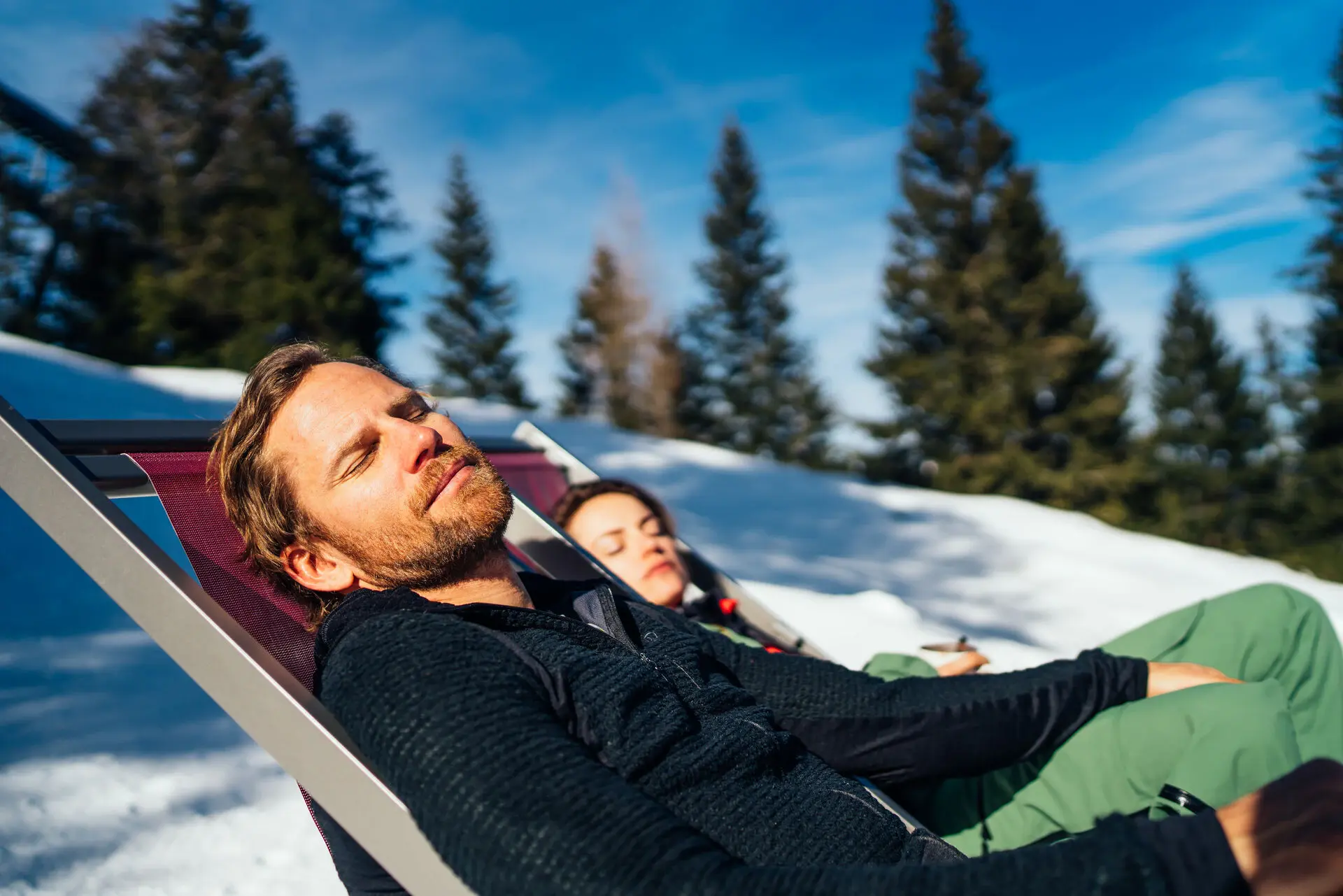 Ein Mann und eine Frau liegen in Stühlen im Schnee.