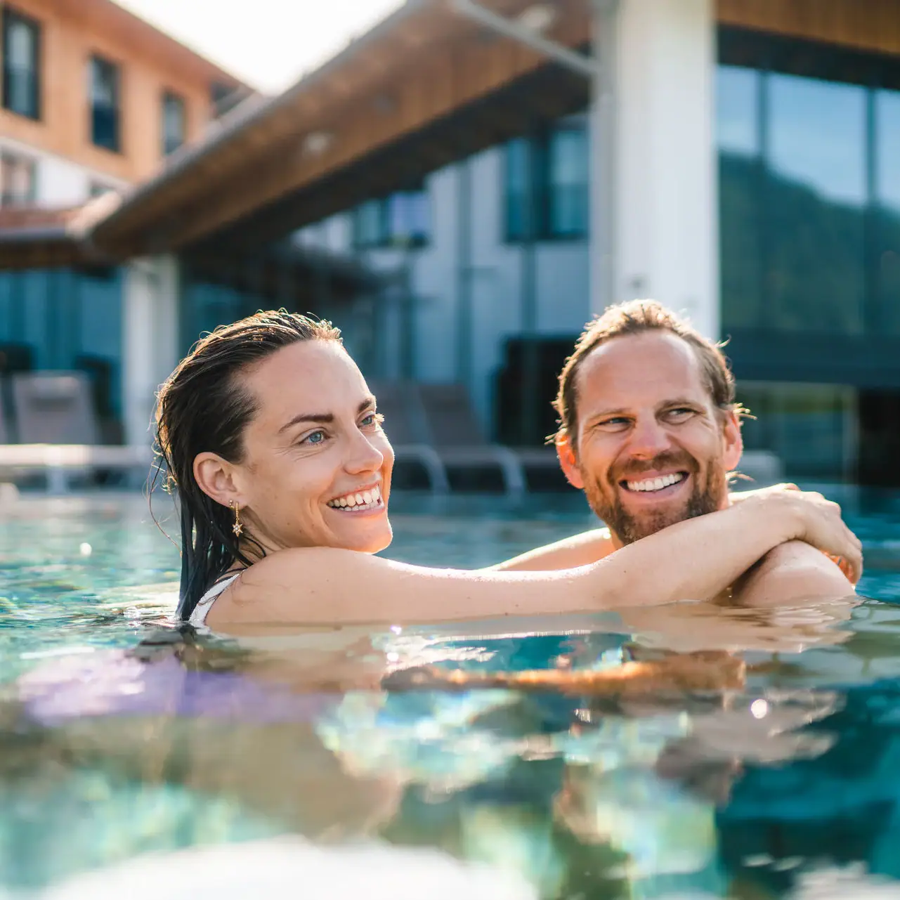 Außenpool im aja Ruhpolding Ein Mann und eine Frau in einem Pool, lächelnd im Wasser.