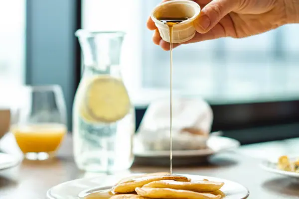 Eine Person gießt Sirup auf einen Teller mit Pfannkuchen.