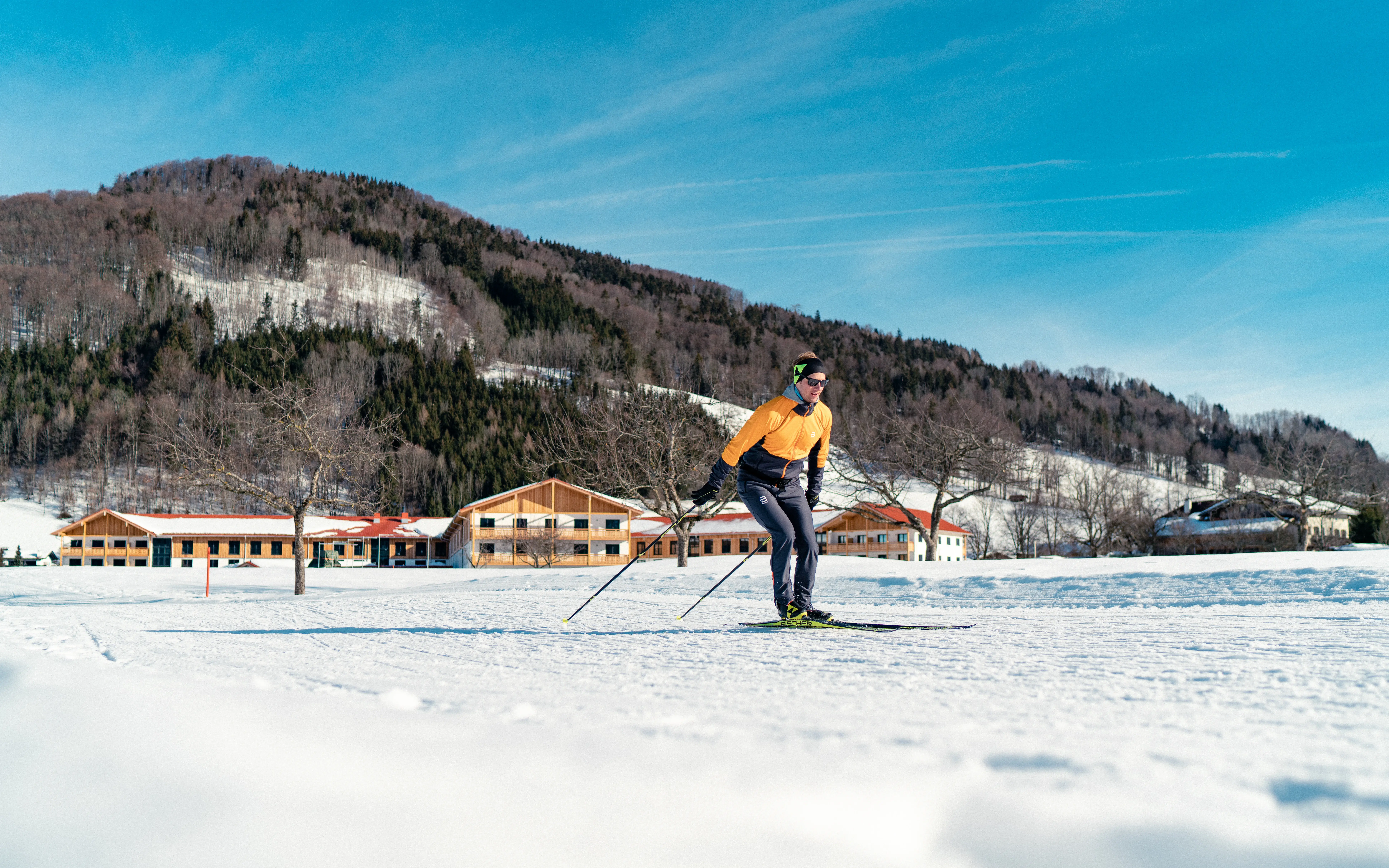Ein Mann beim Skifahren im Schnee, im Hintergrund ist das aja Ruhpolding und eine Berglandschaft