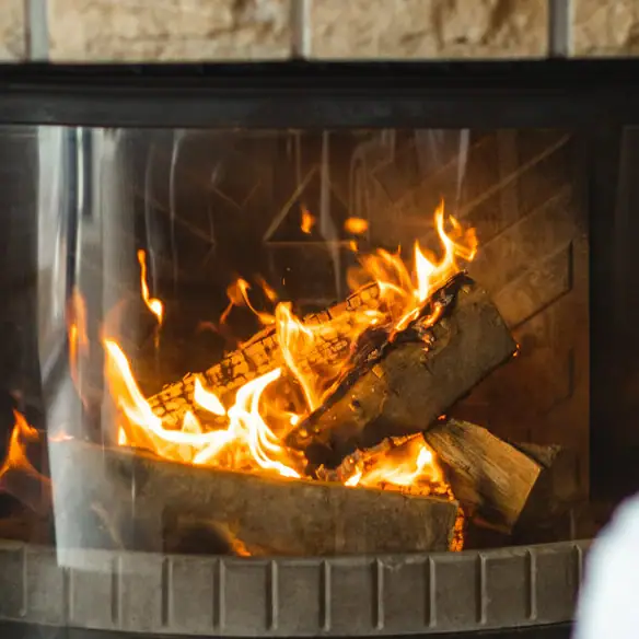 Eine Person hält ein Glas Wein vor einem Kamin.
