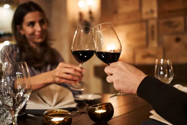 Wein Ein Mann und eine Frau stoßen mit Weingläsern an einem Tisch an.