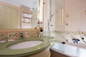 Badezimmer mit Waschbecken und Badewanne, Fliesen an den Wänden, Wasserhahn und Spiegel.