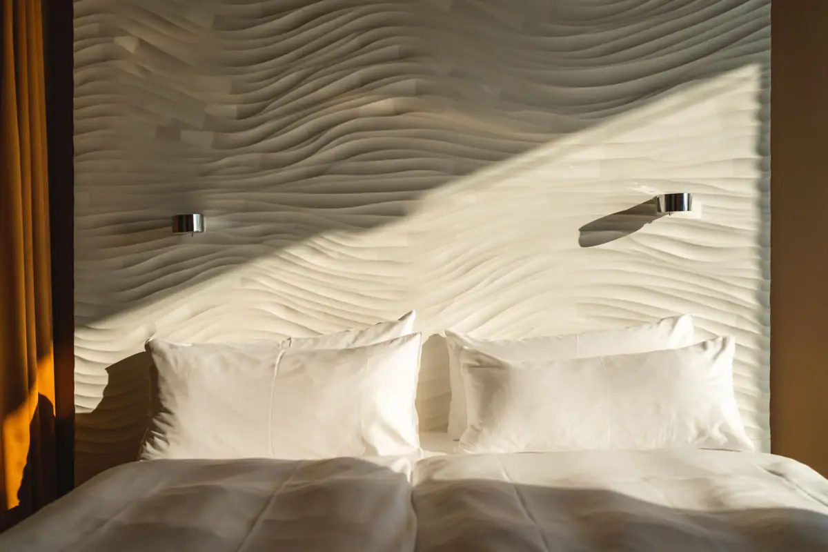 Zimmer im aja Warnemünde Ein Bett mit Kissen vor einer beleuchteten Wand.