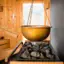 Ein goldener Kessel hängt über einem Saunaofen. Die Holzsauna ist von hellem Tageslicht durchflutet. 