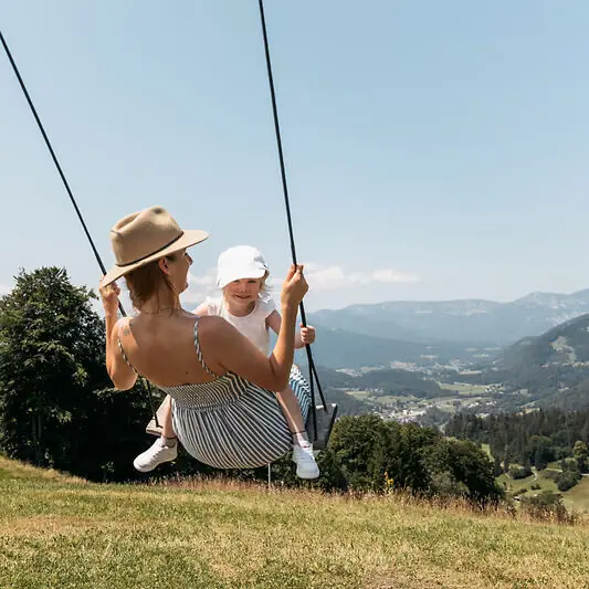 Eine Mutter mit Kind auf einer Schaukel beim Familienurlaub in Ruhpolding.