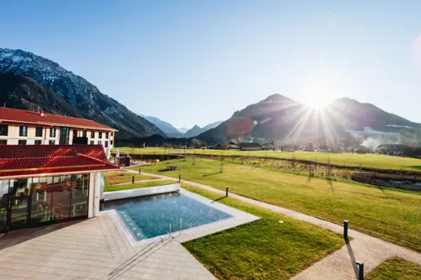 Ein Swimmingpool in einer grasbewachsenen Fläche mit einem Gebäude und Bergen im Hintergrund.