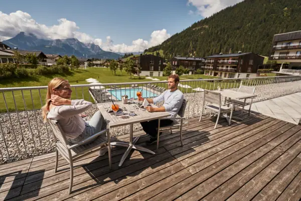 Terrasse mit Bergblick Ein Mann und eine Frau sitzen an einem Tisch auf einem Deck.