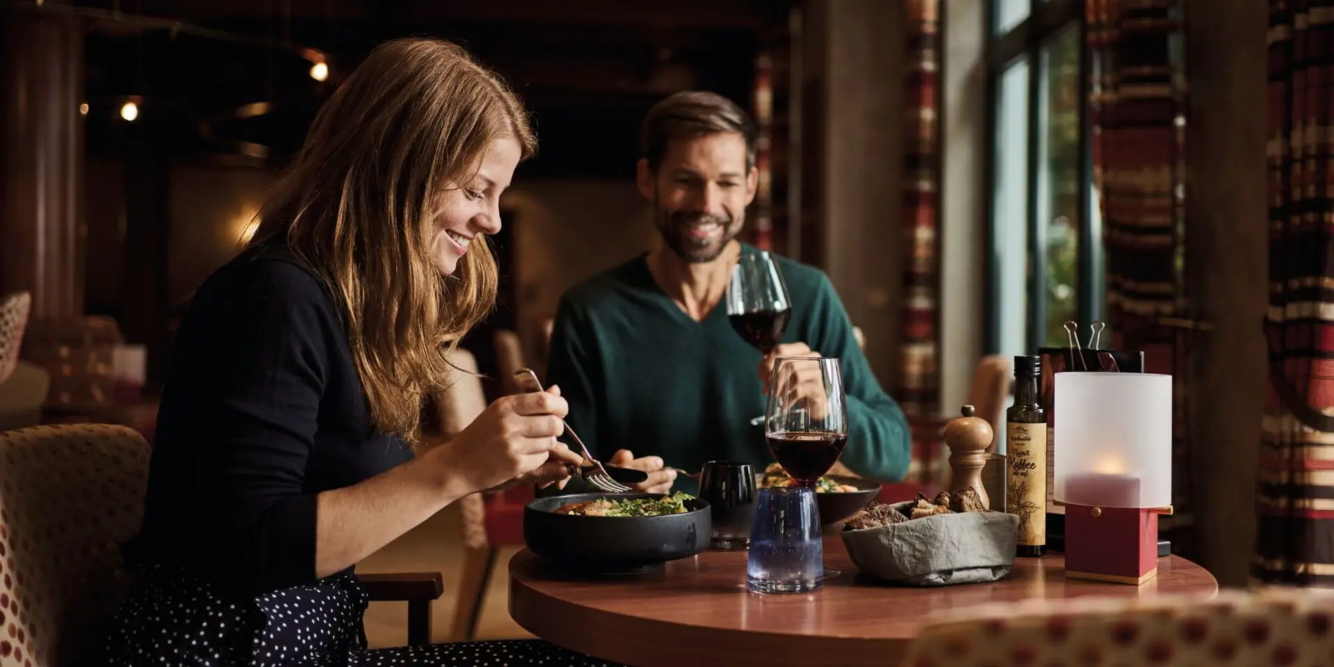 Ein Mann und eine Frau sitzen beim Essen an einem Tisch im Restaurant, mit Weingläsern und einer Flasche Wein.