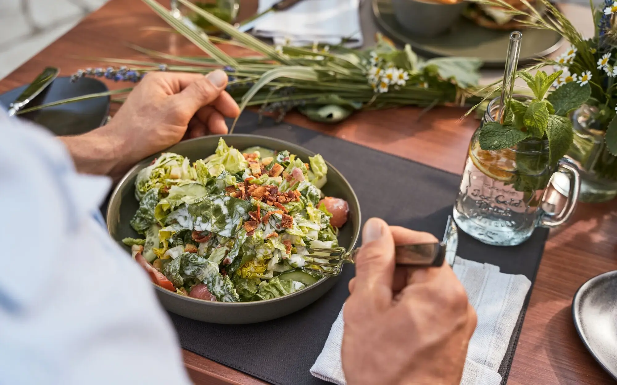 Ein Mensch isst einen Salat an einem gedeckten Tisch.