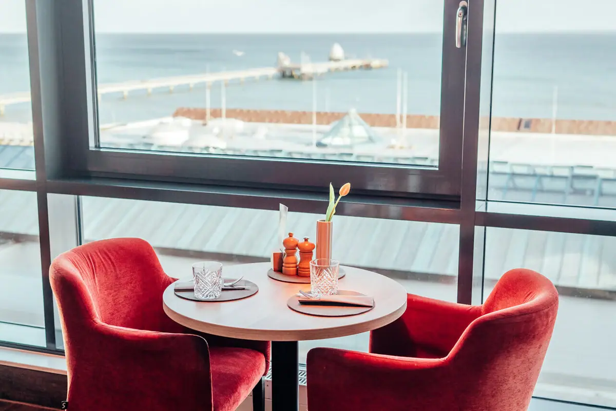 JEDERMANNS Restaurant Grömitz Ein Tisch mit roten Stühlen und mit Aussicht auf die Ostsee