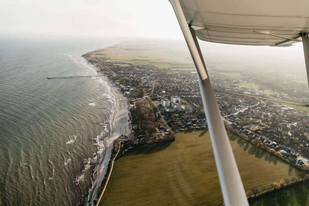 Blick über Grömitz Luftaufnahme eines Strandes und Landes mit Wasser im Vordergrund.