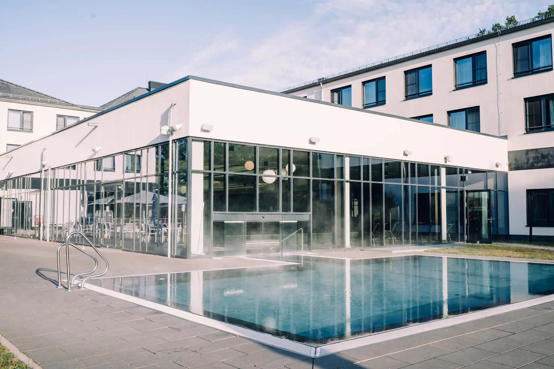 aja SPA Bad Saarow Ein Gebäude mit einem Pool im Vordergrund und Fenstern im Hintergrund.