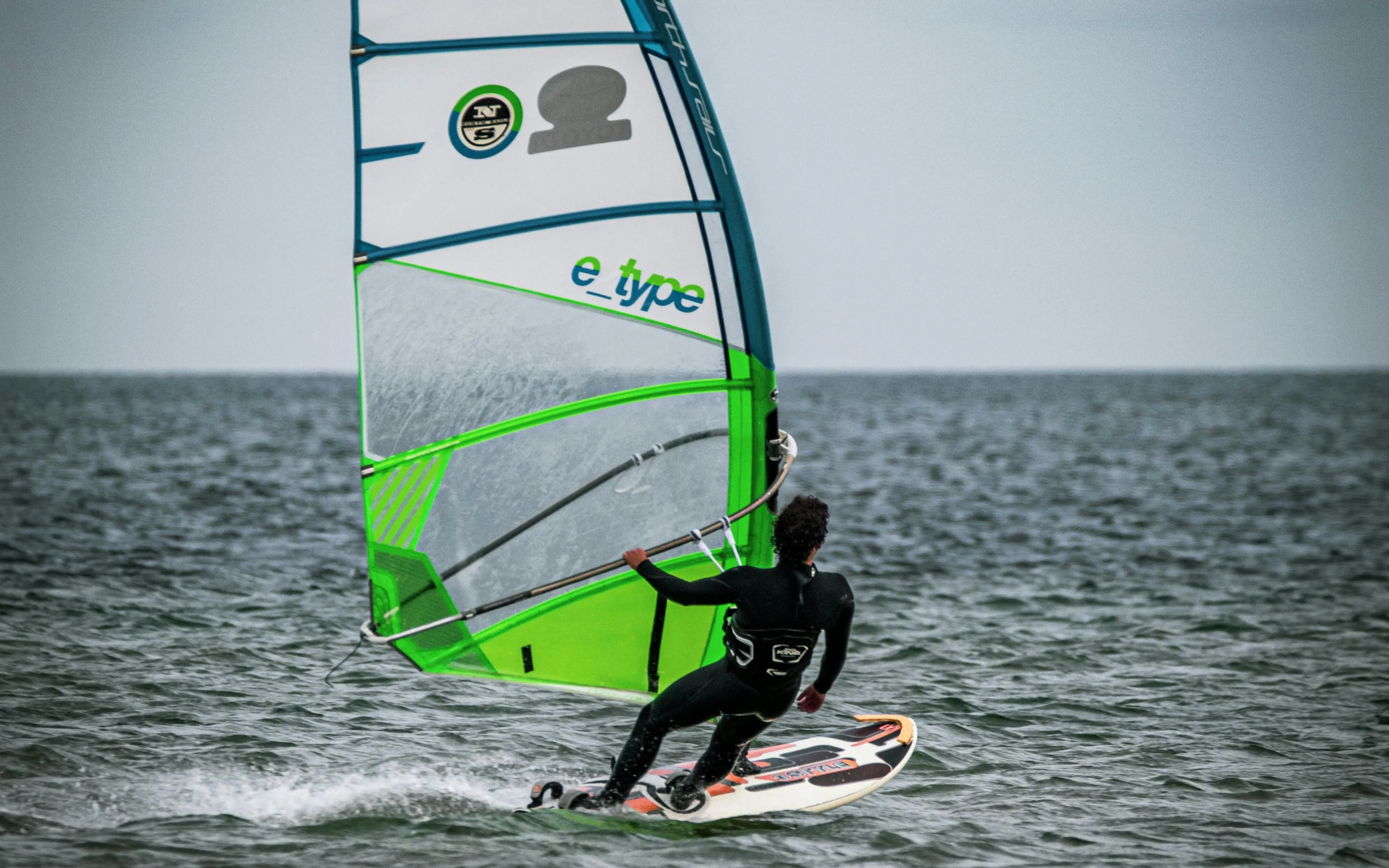 Person windsurfing on a surfboard with a green sail.