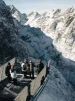 Gruppe von Personen auf einer Aussichtsplattform über einem verschneiten Gebirge.