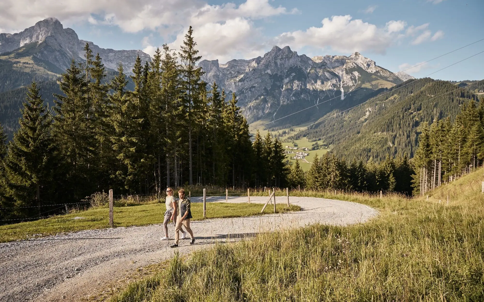 Zwei Personen gehen auf einem Schotterweg vor einer Bergkette.