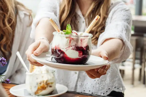 Eine Frau hält einen Teller mit einem Eisbecher mit Vanilleeis und Kirschen..