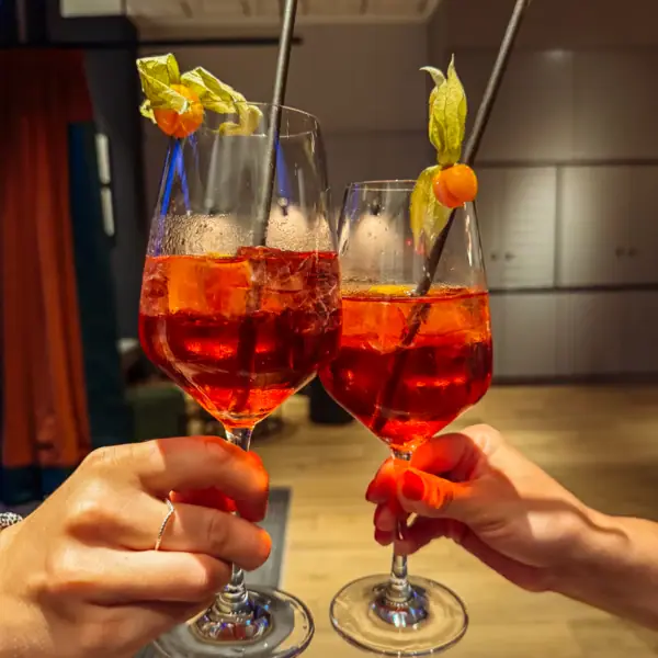 Hände halten Gläser mit orangefarbenem Getränk und Strohhalmen.