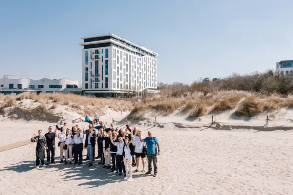 Eine Gruppe aus Menschen vom Team des Hotels posiert für ein Foto vor dem aja Warnemünde Gebäude.