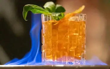 Ein Cocktail im Old Fashioned Glas mit Eiswürfeln, der in Flammen steht.