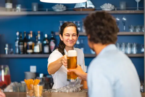 aja Bar Warnemünde Eine Frau hält ein Glas Bier an der Bar und übergibt es einem Gast.