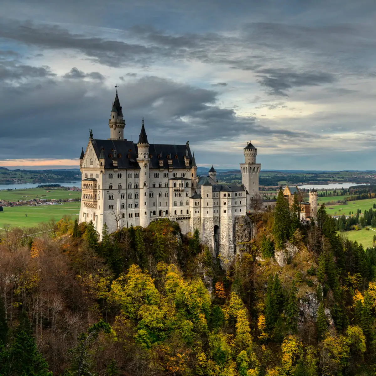 Das Schloss Neuschwanstein auf einem Hügel mit herbstlichen Bäumen im Vordergrund.