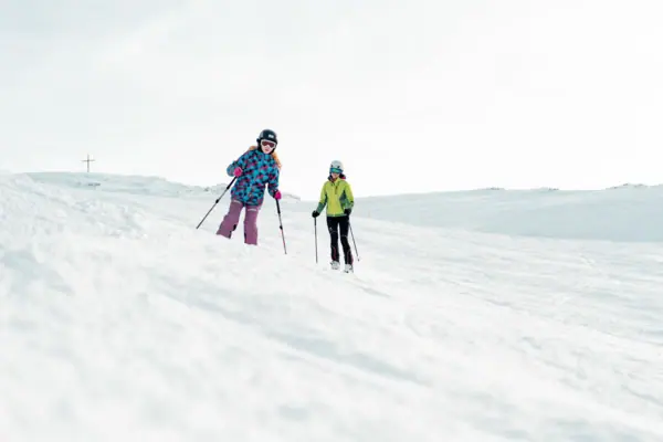 Zwei Personen beim Skifahren auf einem verschneiten Hügel.